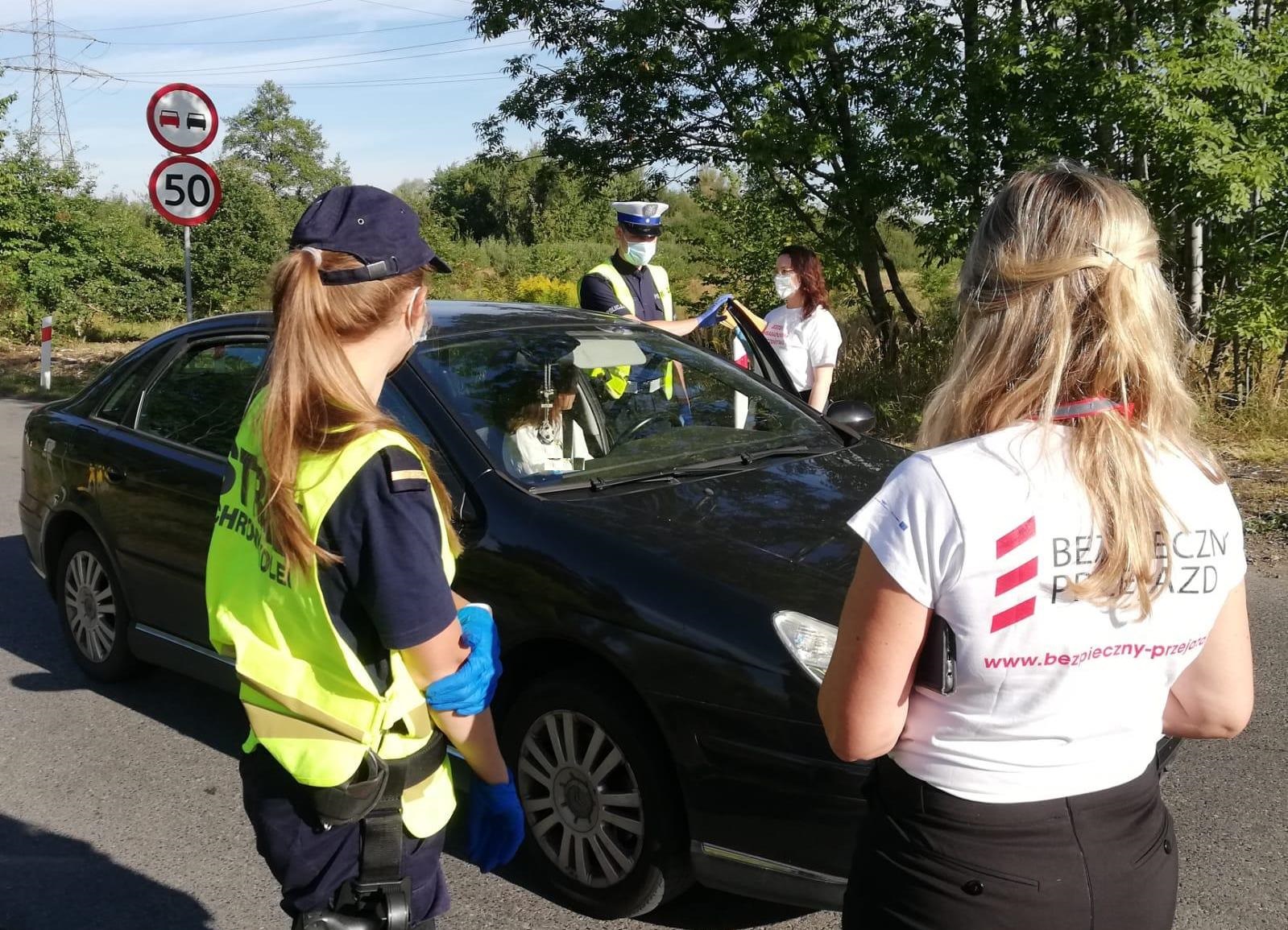 KPP Oświęcim ostatnia wakacyjna akcja Bezpieczny przejazd policjant oraz przedstawicielki kolei rozmawiaja z kierowcami